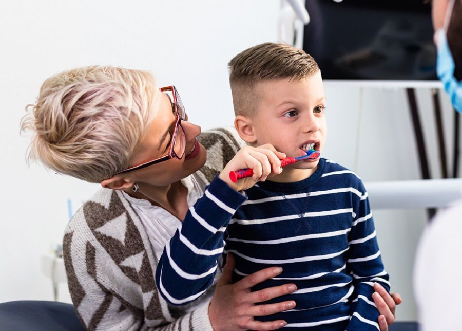 A woman is brushing a young boy 's teeth with a toothbrush.