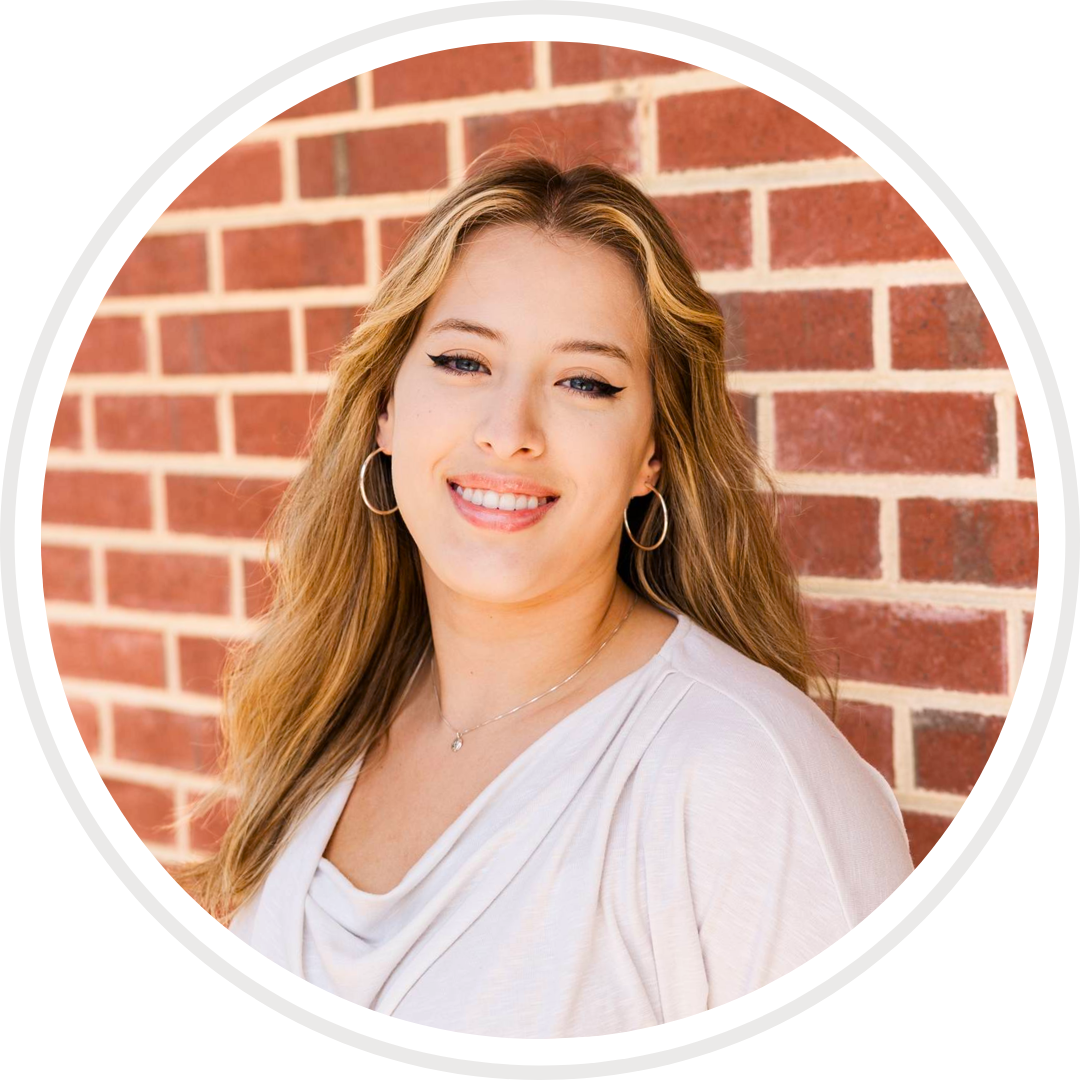 A woman is smiling in front of a brick wall