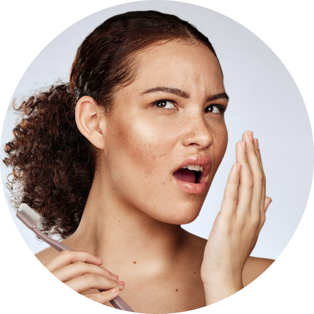 A woman covering her mouth with her hand while holding a toothbrush