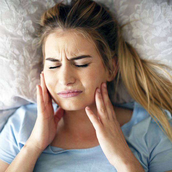 A woman is laying in bed with her eyes closed and her hands on her face.