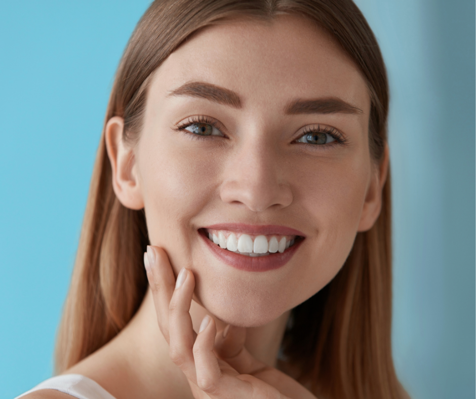 A woman is smiling and touching her face with her hand.