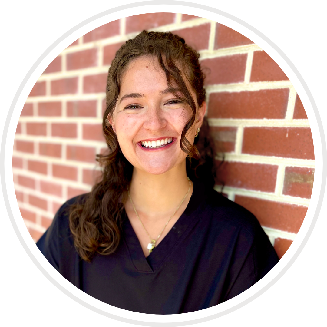 A woman is smiling in front of a brick wall.