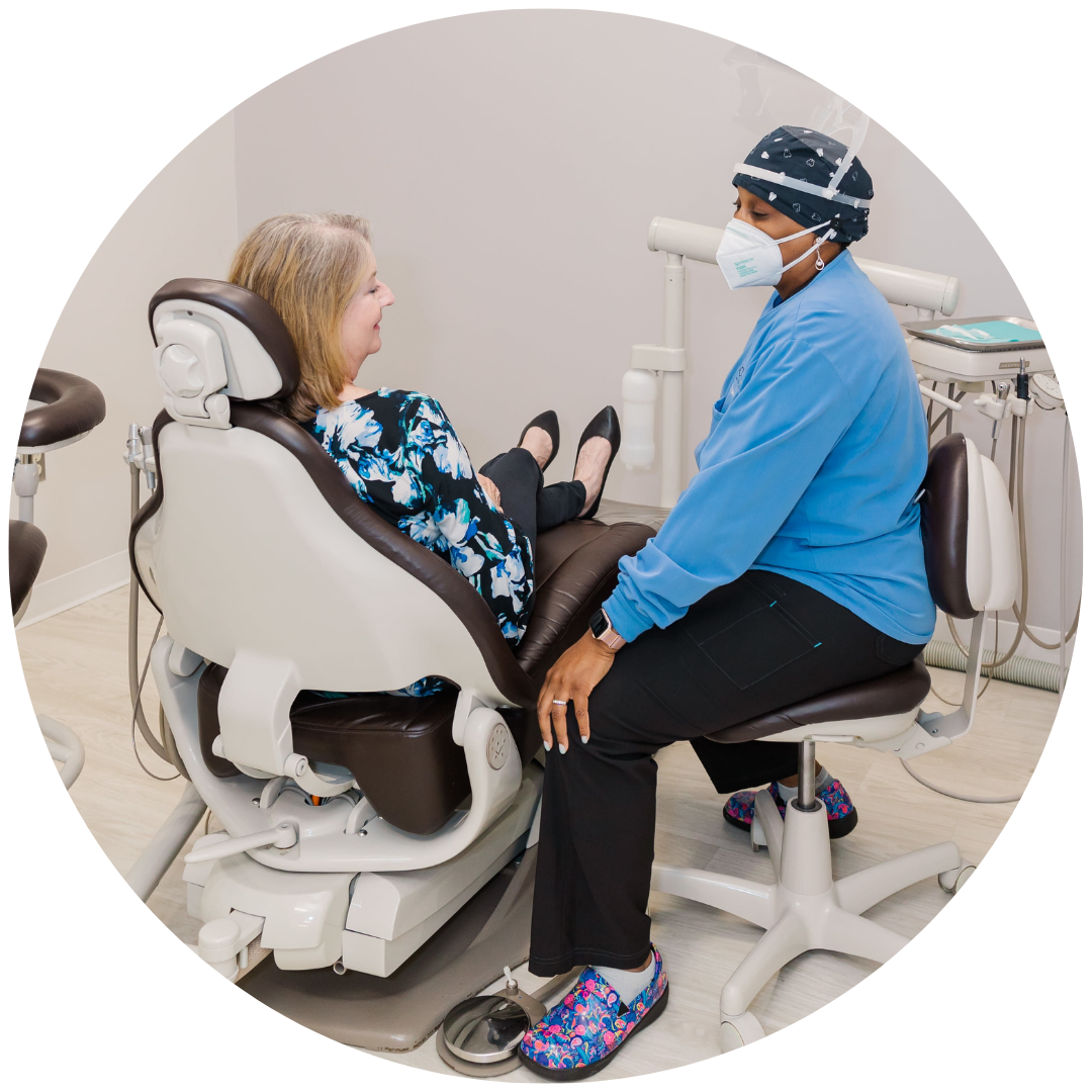 A woman is sitting in a dental chair talking to a dentist wearing a mask.