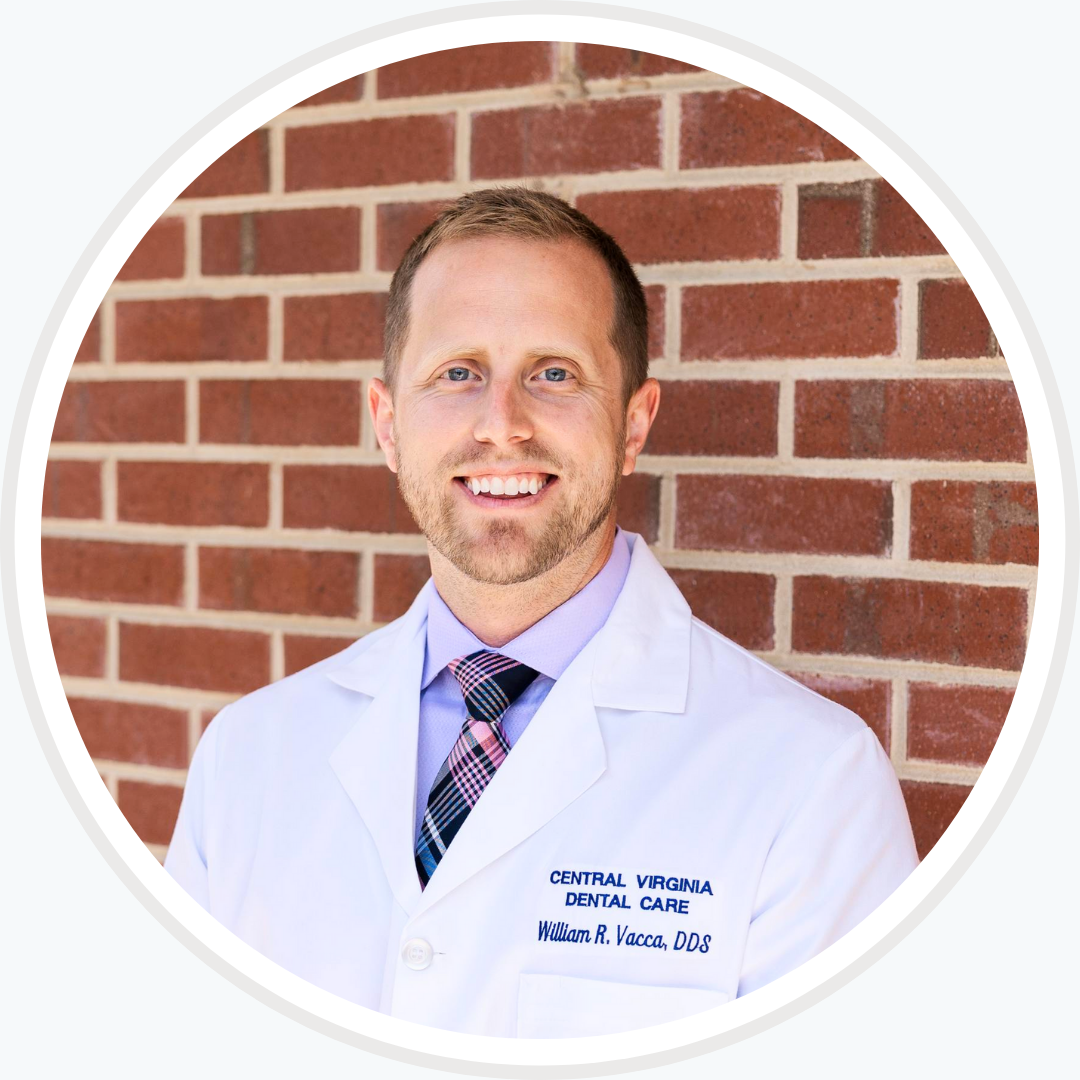 A man in a lab coat and tie is smiling in front of a brick wall
