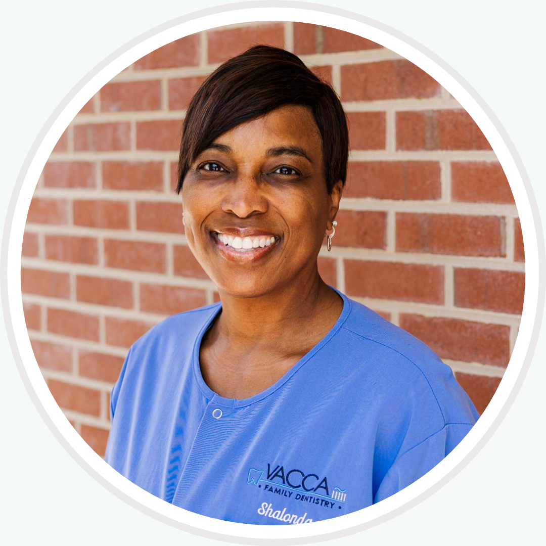 A woman wearing a blue shirt that says vacca smiles in front of a brick wall