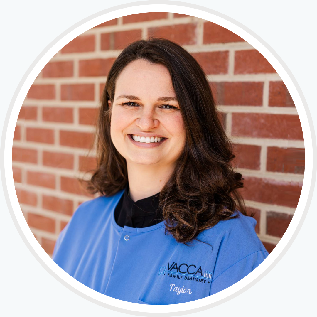 A woman in a blue shirt is smiling in front of a brick wall.