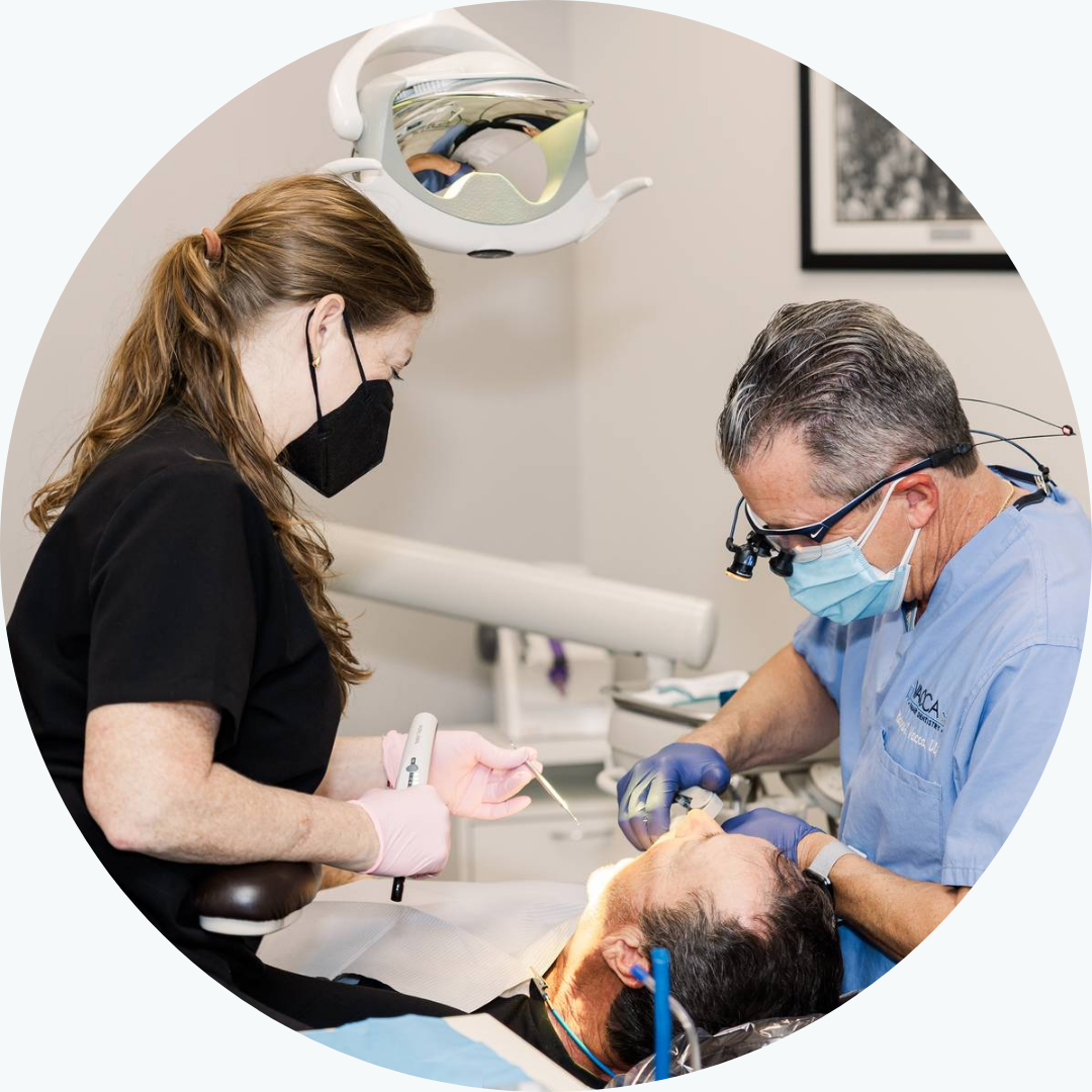 A woman is sitting in a dental chair talking to a dentist wearing a mask.