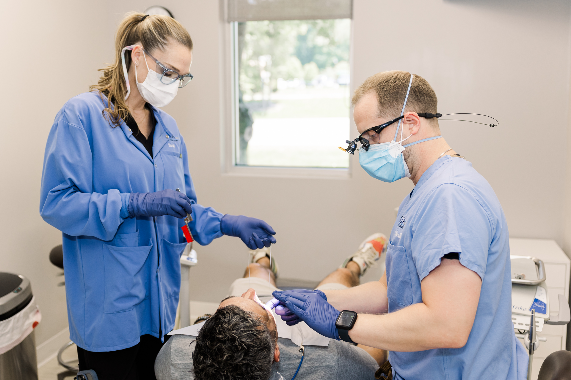 Two dentists are examining a patient 's teeth in a dental office.