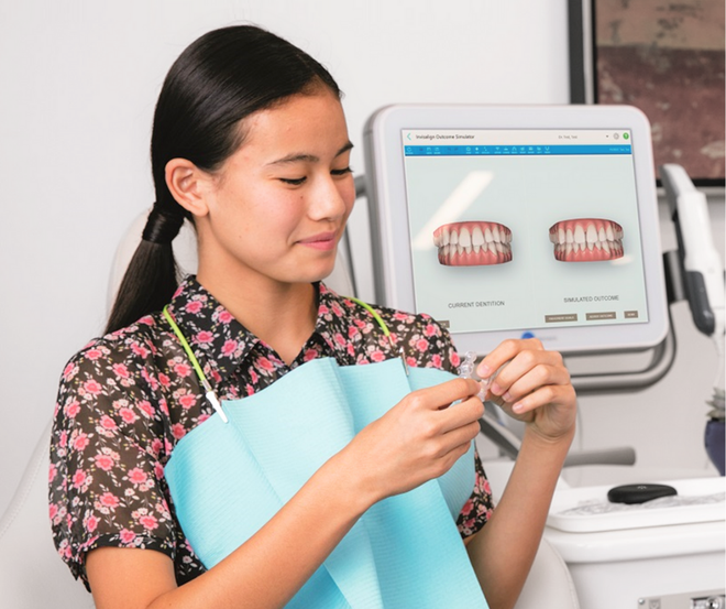 A woman in a floral shirt is looking at her teeth on a screen