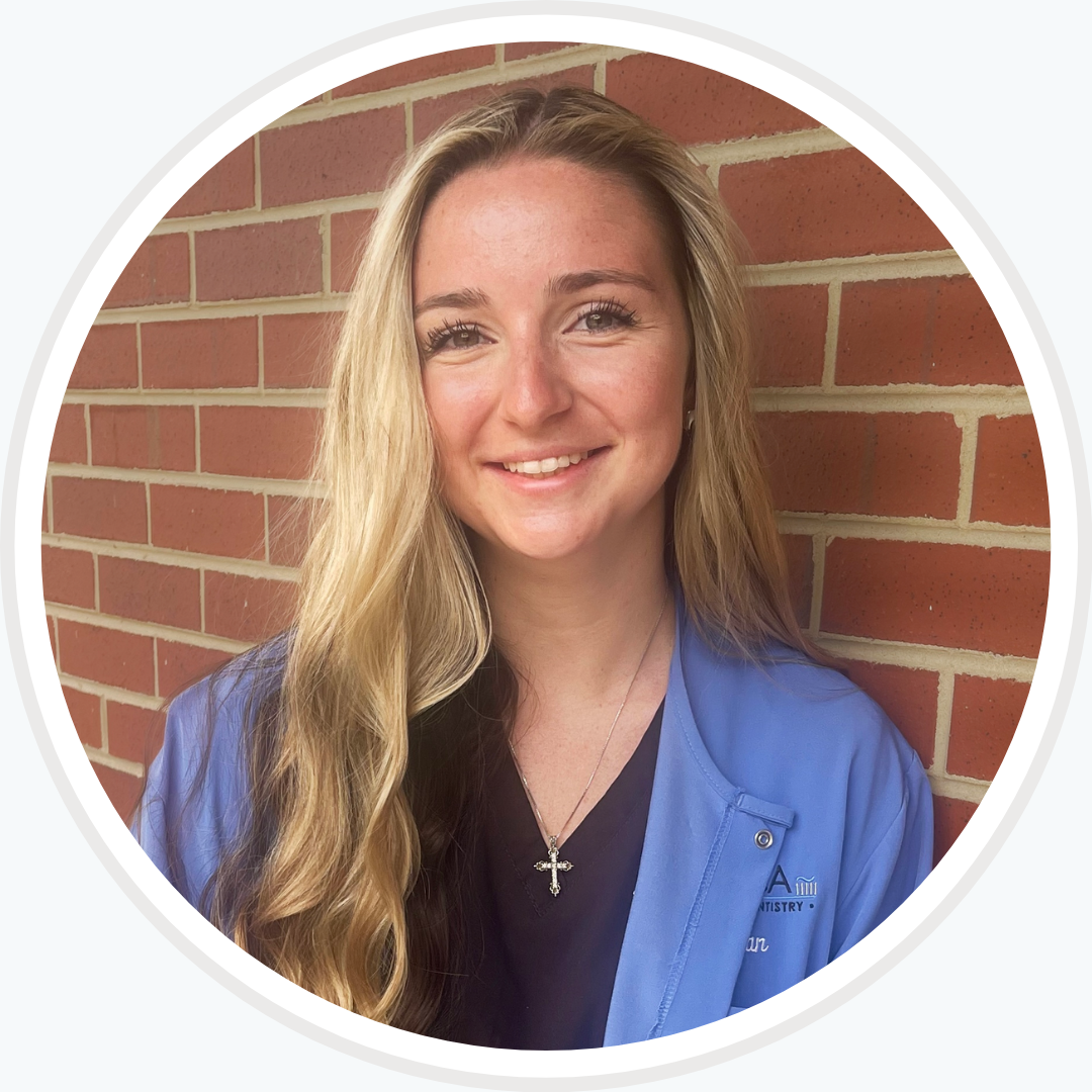 A woman in a blue shirt is smiling in front of a brick wall.