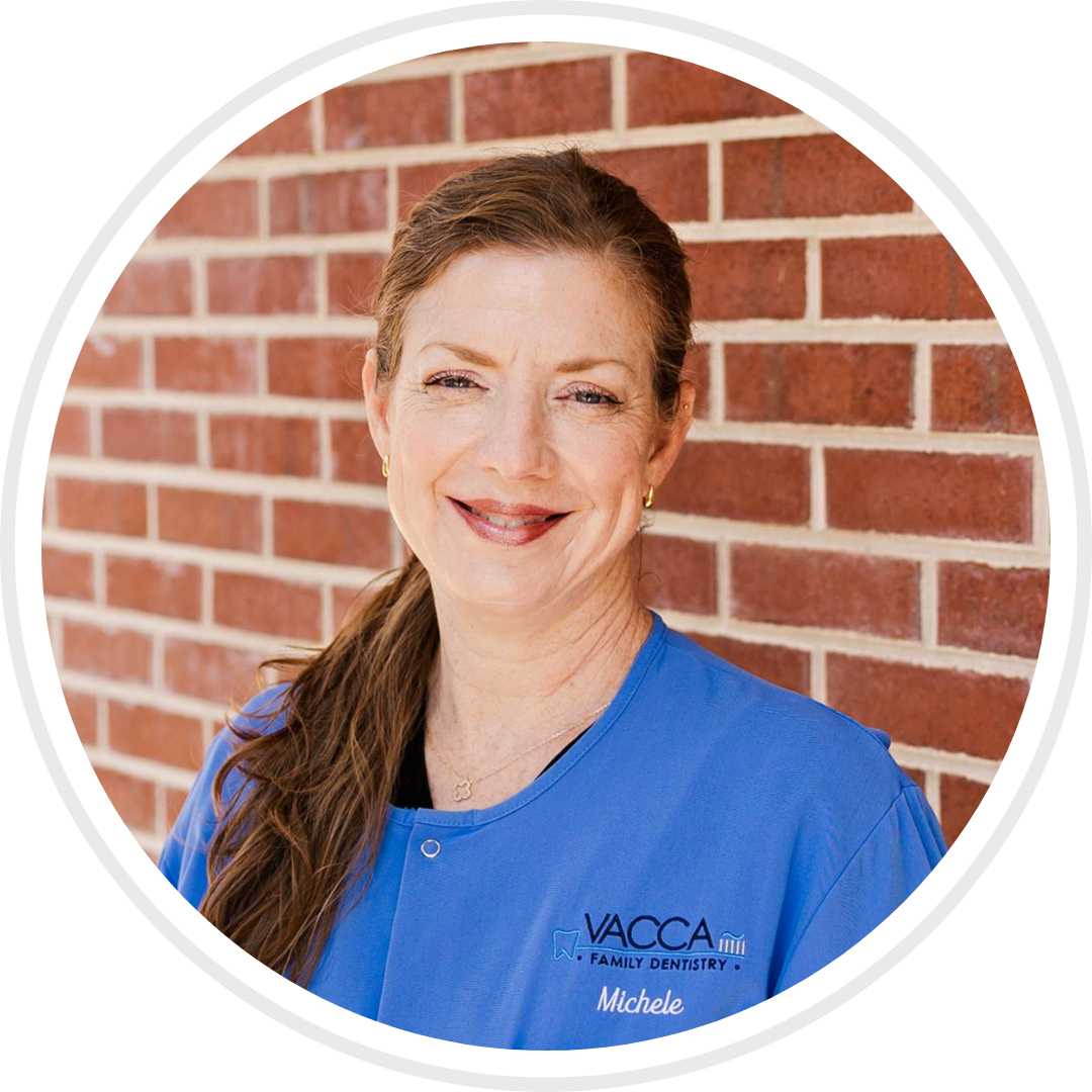 A woman in a blue jacket is smiling in front of a brick wall.