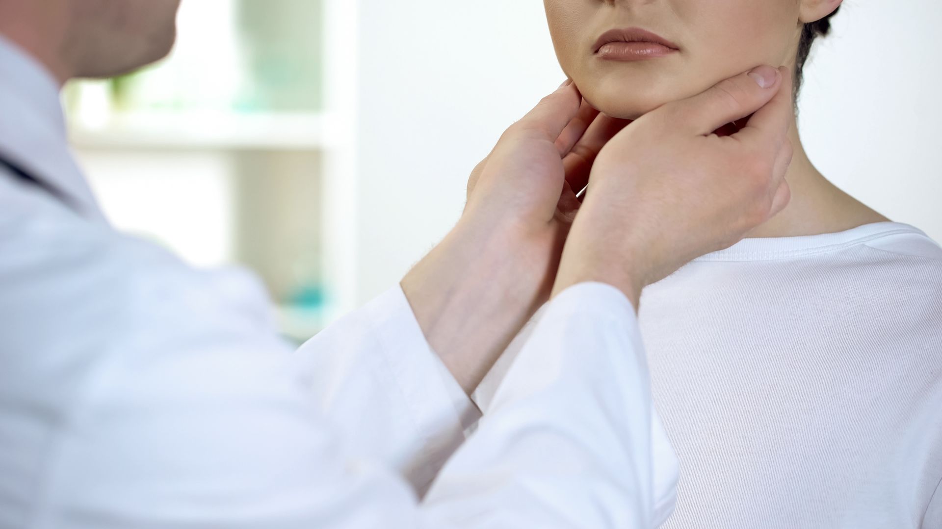 Doctor examining a patient's neck, likely checking for oral  thyroid The doctor wears a w