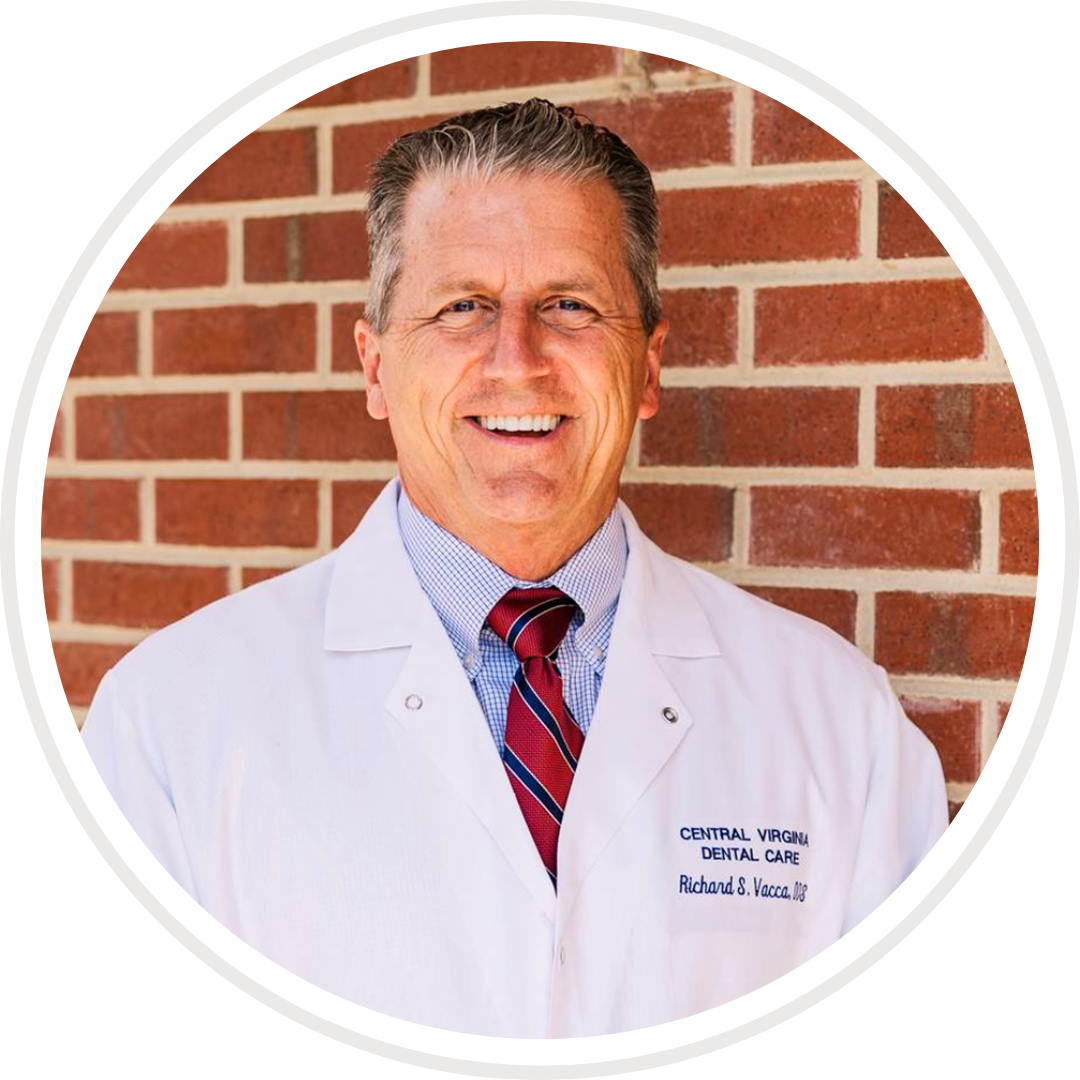 A man in a lab coat and tie is smiling in front of a brick wall