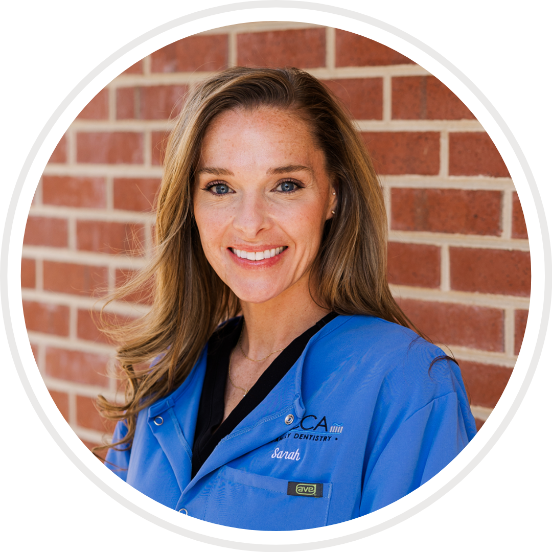 A woman in a blue coat is smiling in front of a brick wall.