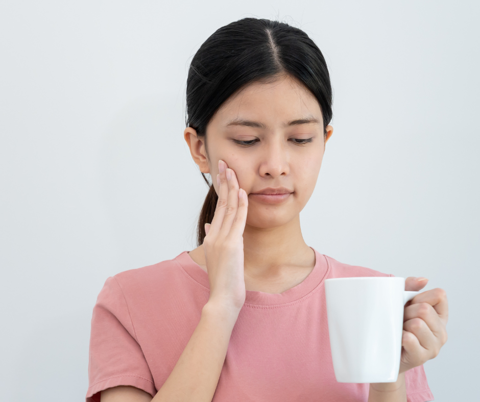 Woman holding a mug, touching her cheek with a pained expression.
