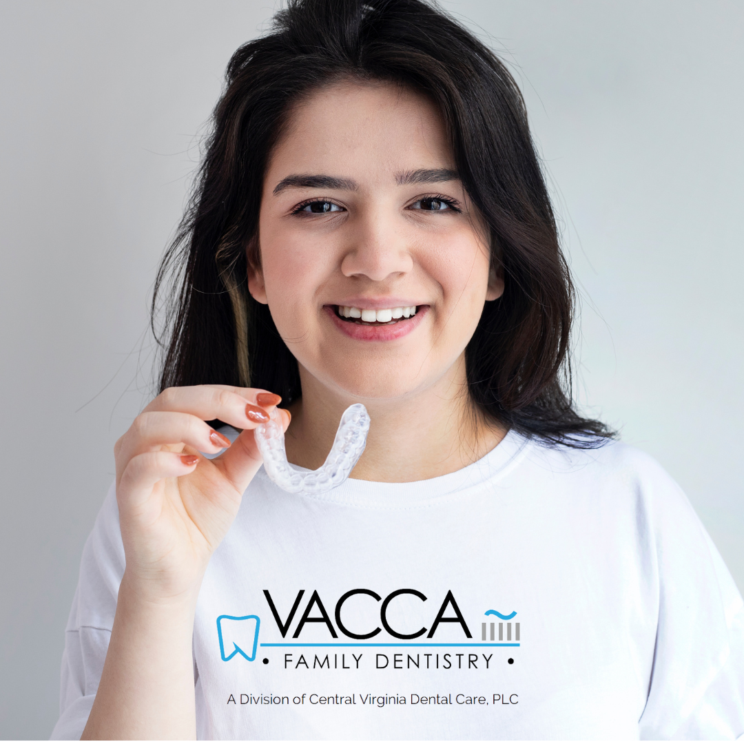 A woman wearing a vacca family dentistry t-shirt is holding a dental retainer.