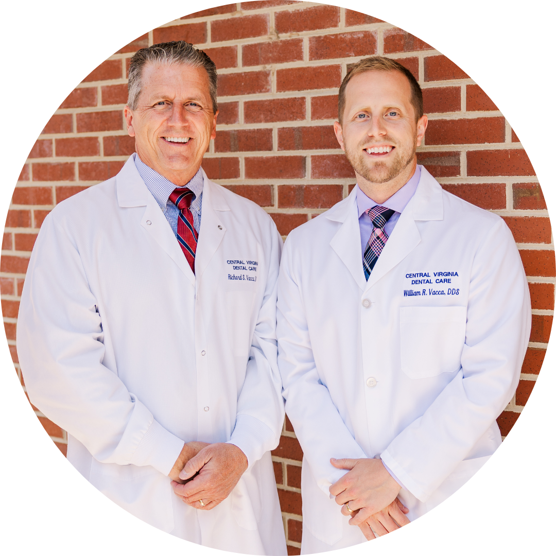 Two men, Dr. Richard Vacca and Will Vacca Vacca in white coats and ties are standing in front of a brick wall