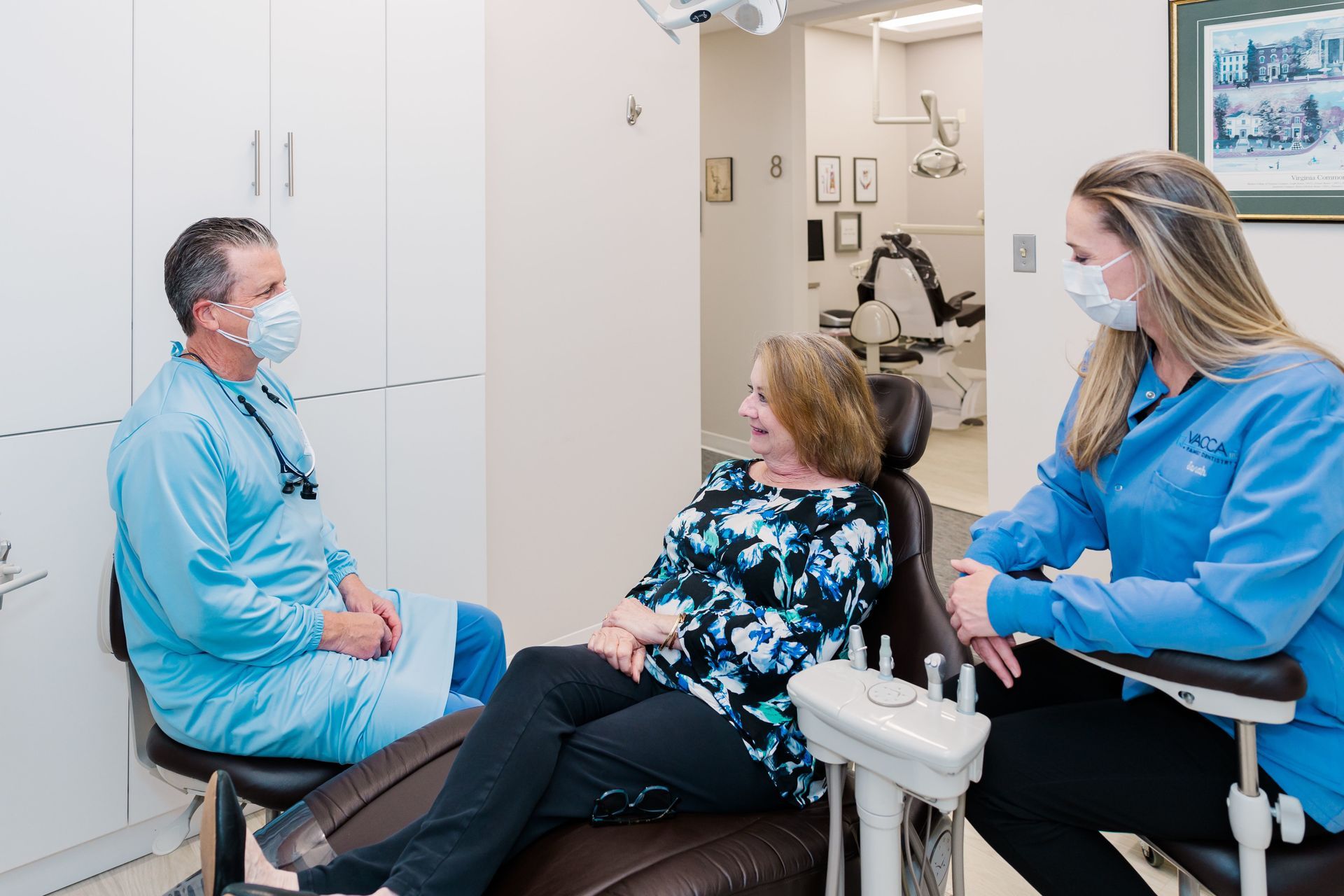 A woman is sitting in a dental chair talking to a dentist and a nurse.