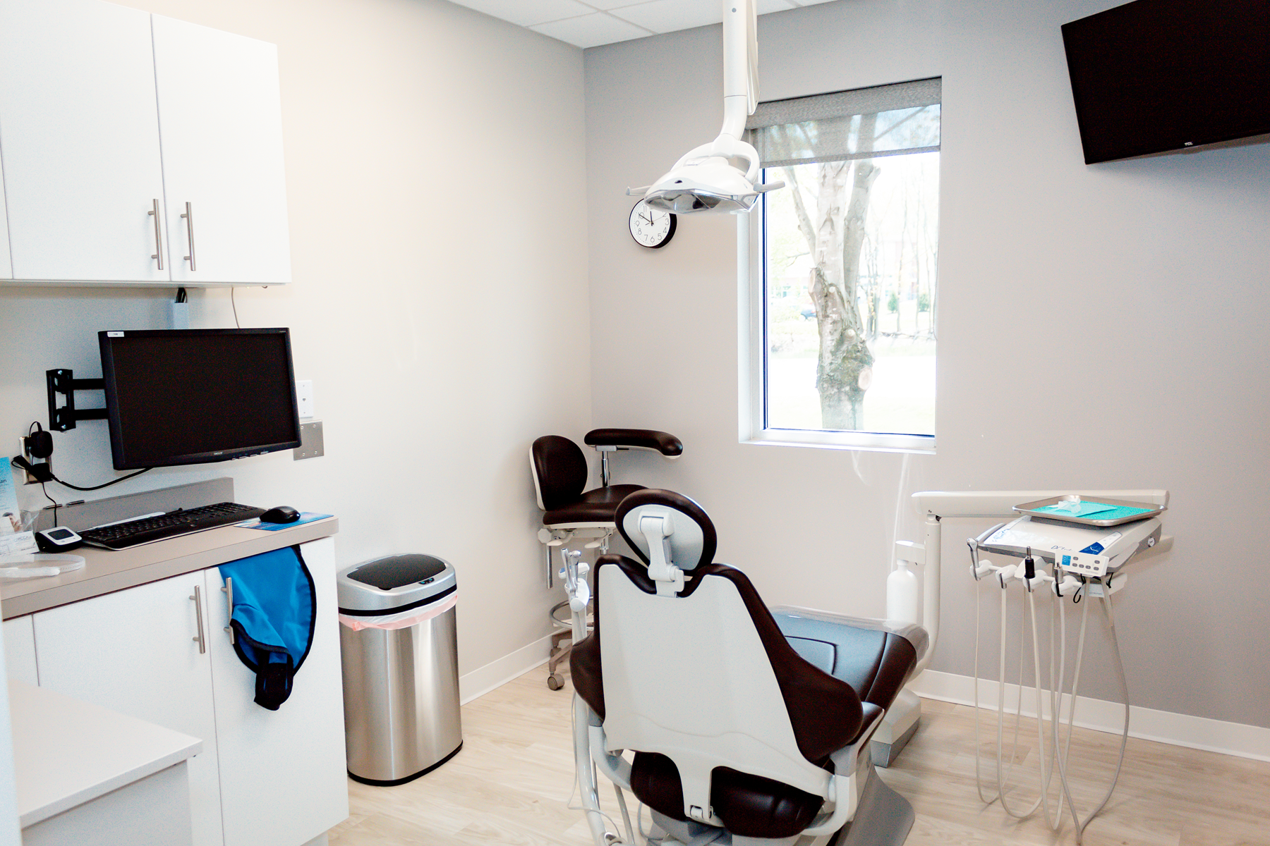 Dental exam room with chair, overhead light, computer, sink, and medical cart