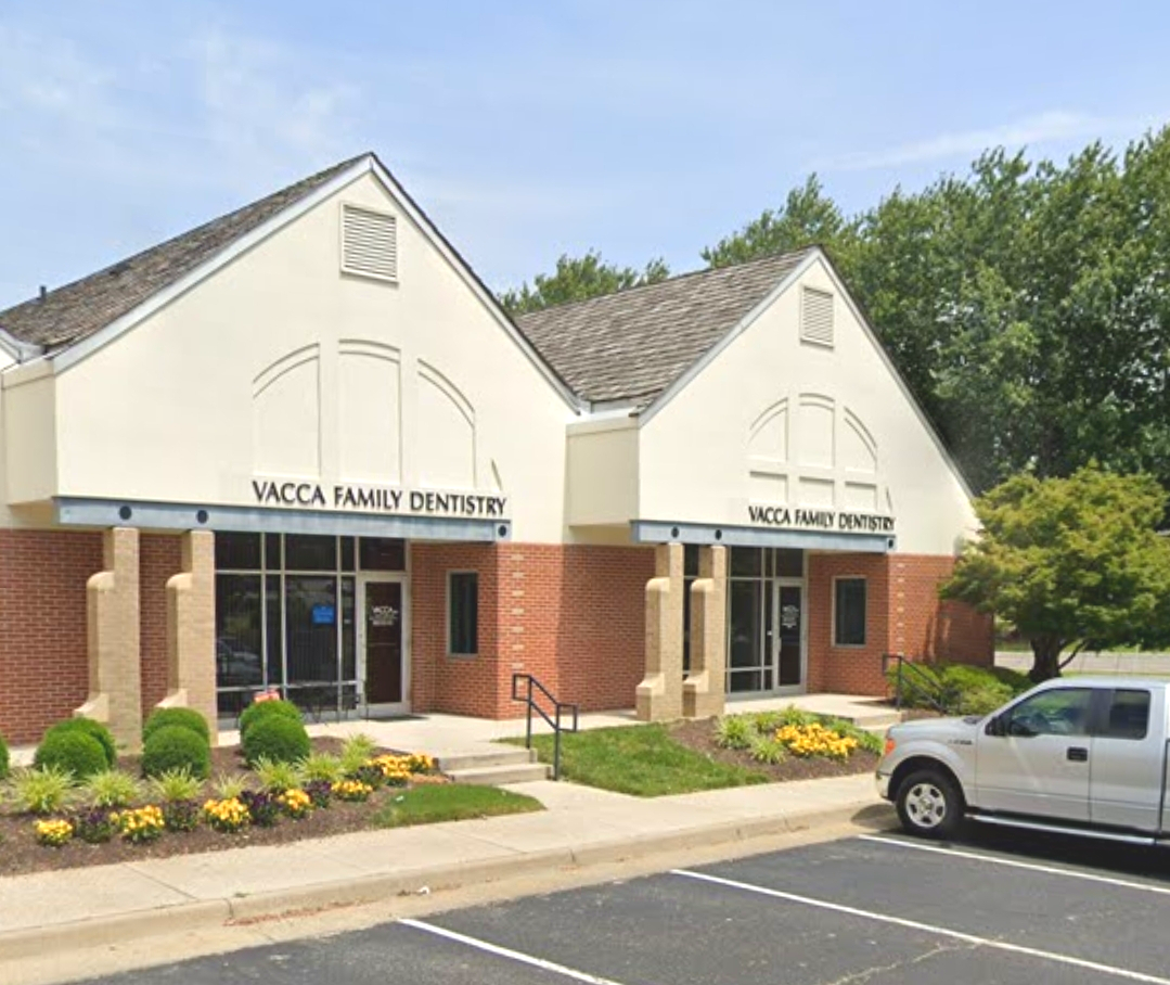 Exterior of a dental office with white peaked roof, brick facade, landscaped entrance, and a parked silver truck