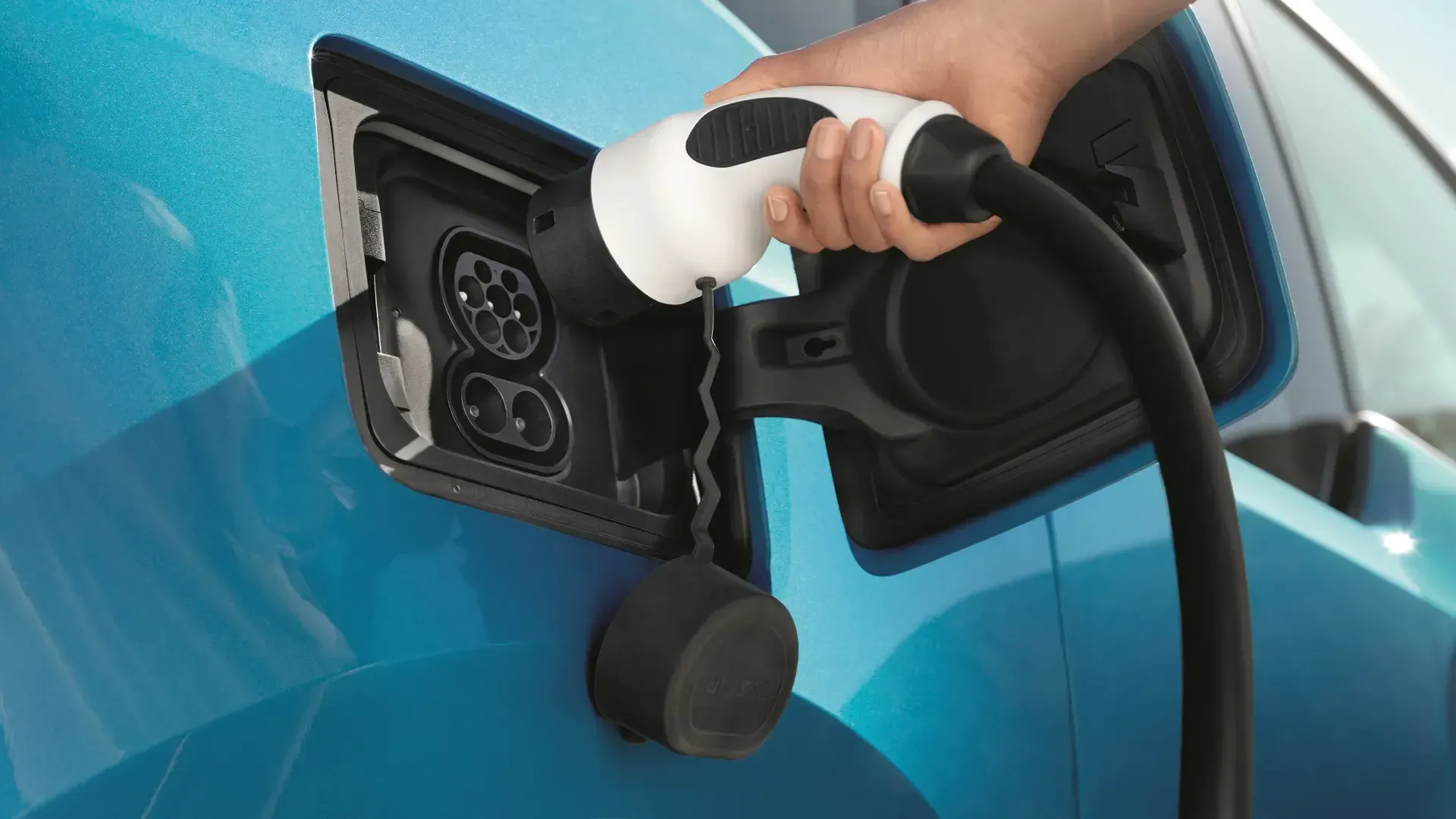 Hand plugging an electric vehicle charging cable into a blue car.