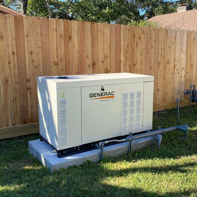 A Generac generator on a concrete pad next to a wooden fence.