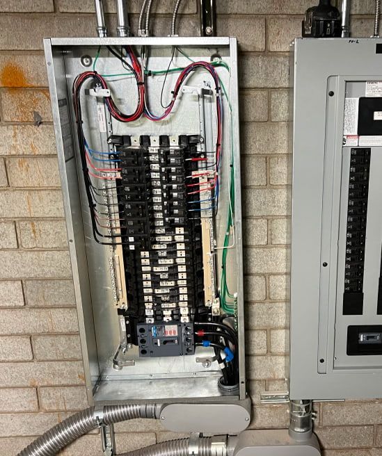 Open electrical panel with wires and circuit breakers, mounted on a brick wall.