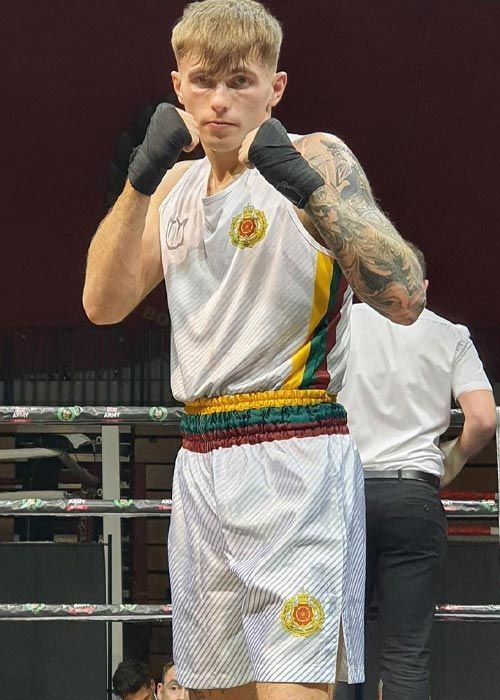 A man is standing in a boxing ring wearing a white shirt and shorts.