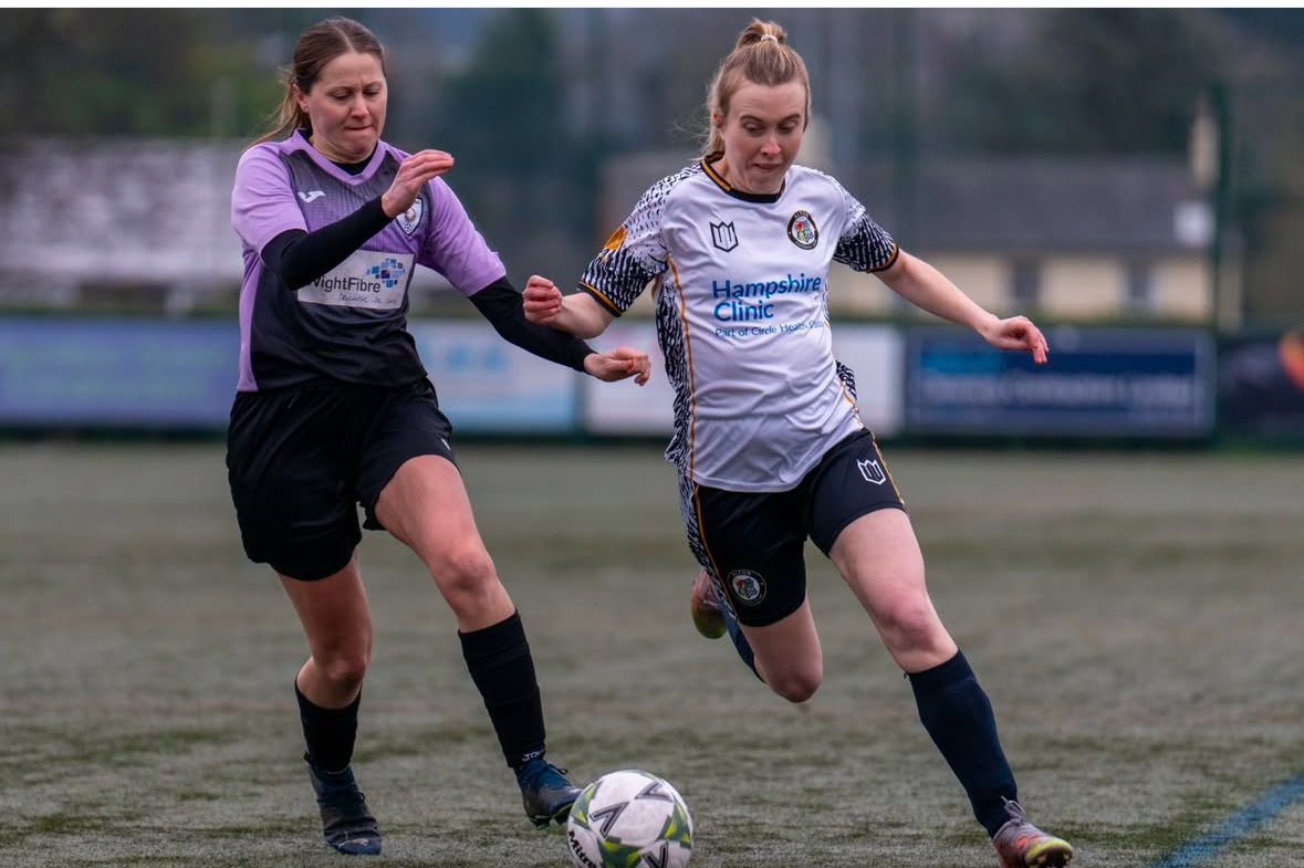 Two female soccer players are playing soccer on a field.