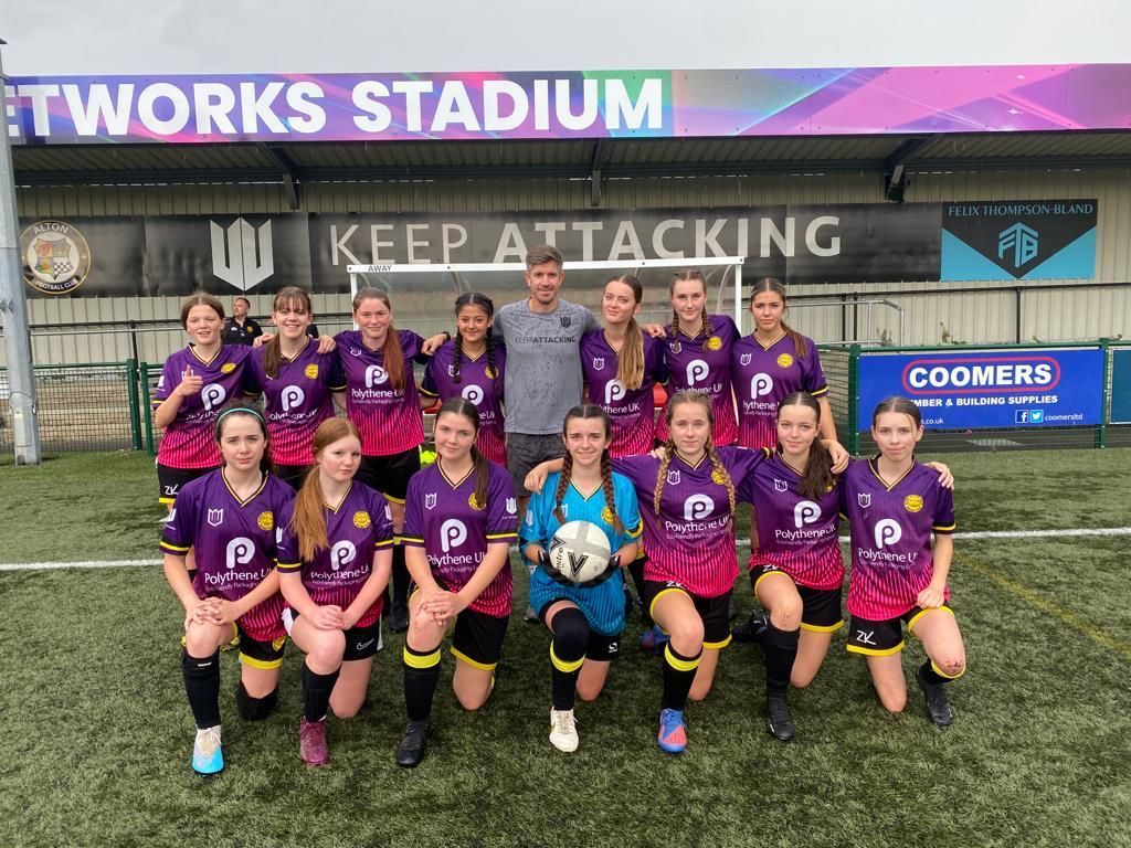 A group of young girls are posing for a picture on a soccer field.