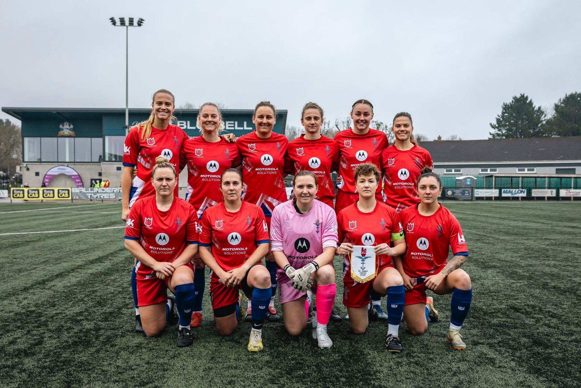 A group of female soccer players are posing for a team photo on a field.