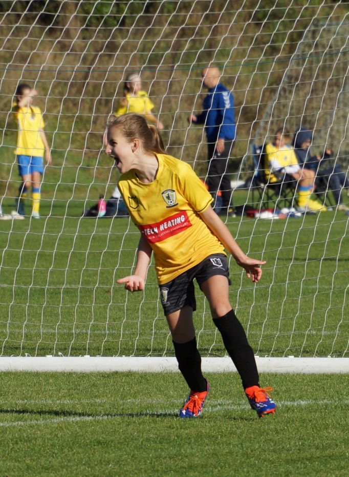 A young girl in a yellow jersey is playing soccer on a field.