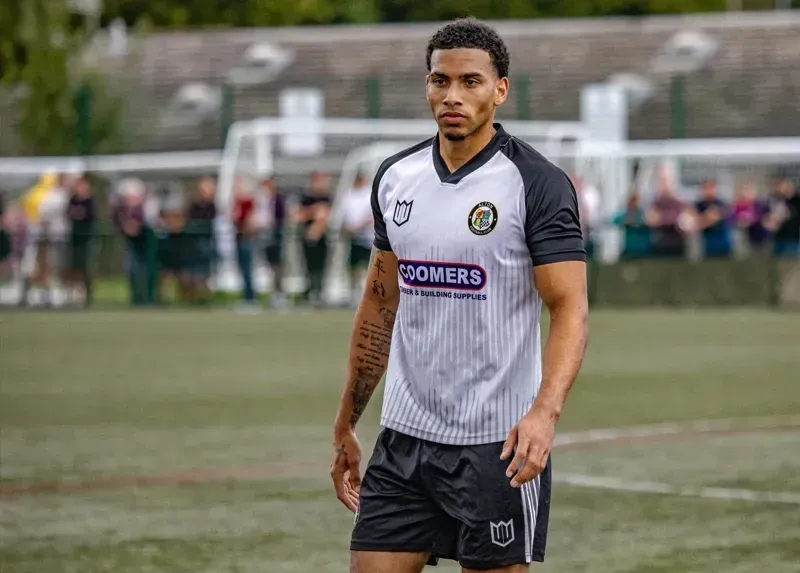 A soccer player is standing on a field wearing a white and black jersey.