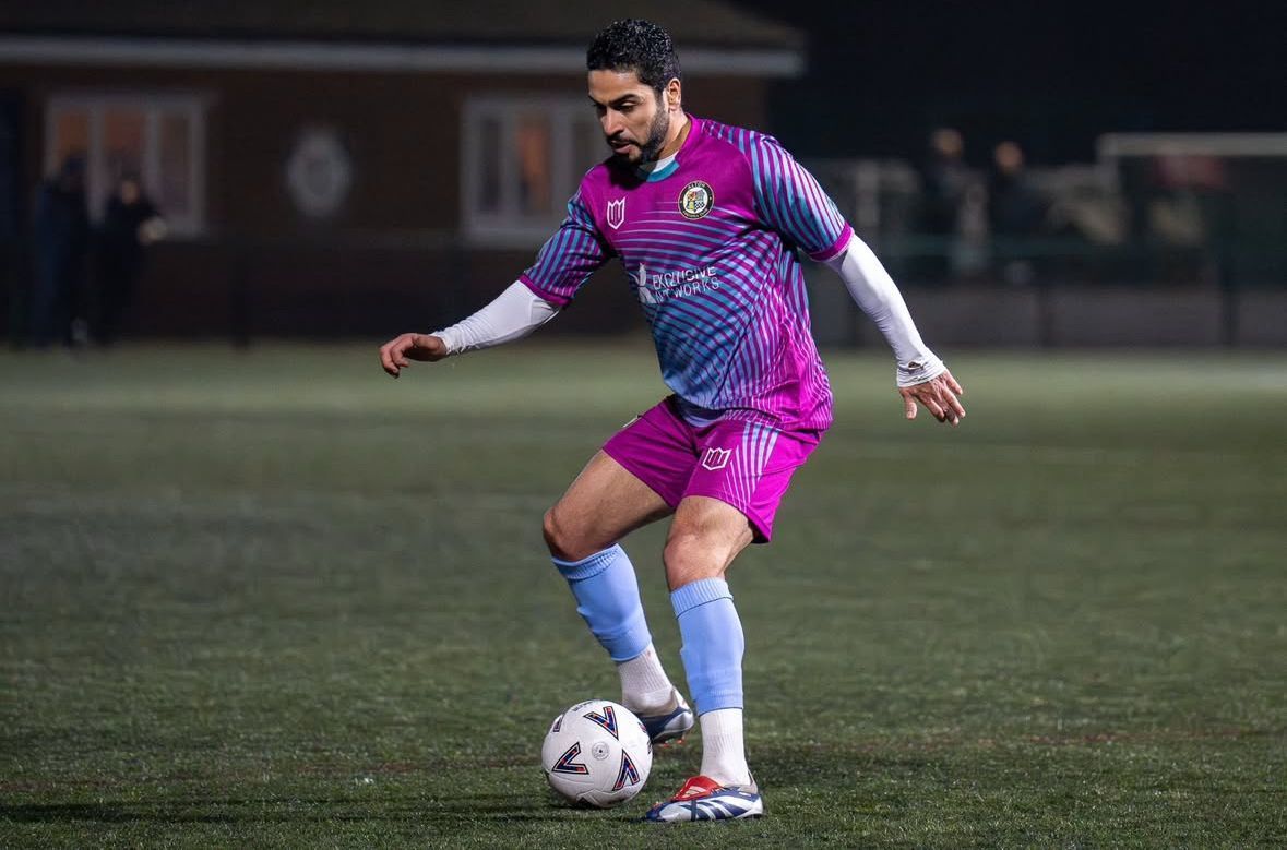 A soccer player in a purple and blue uniform is kicking a soccer ball on a field.