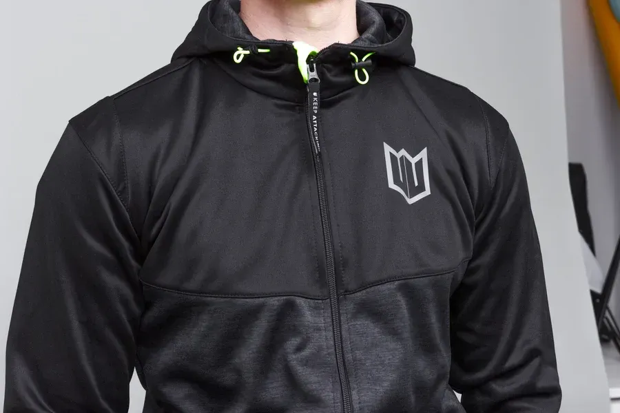 A man wearing a black hoodie and grey sweatpants is standing with his hands in his pockets.