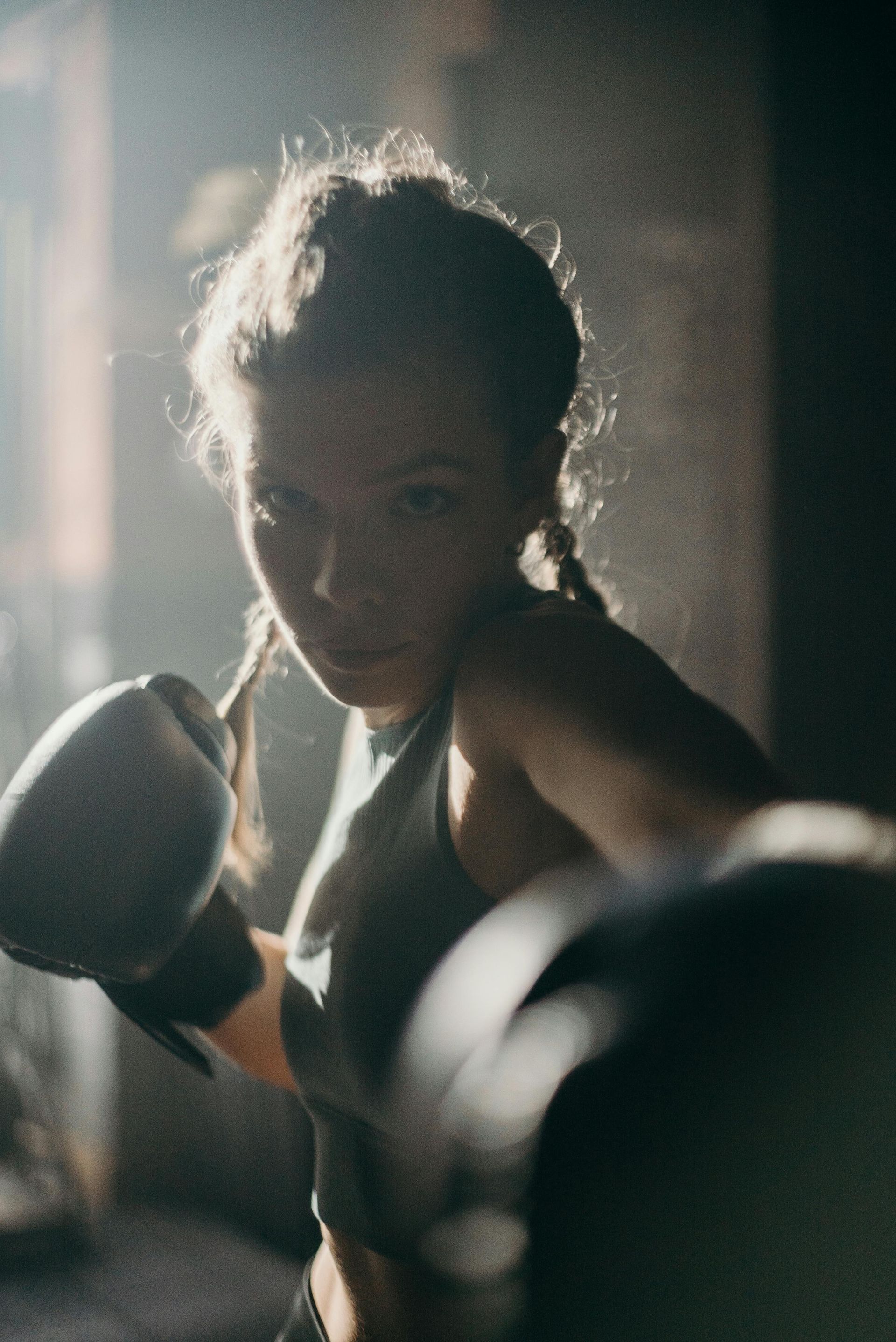 A young girl is wearing boxing gloves in a dark room.