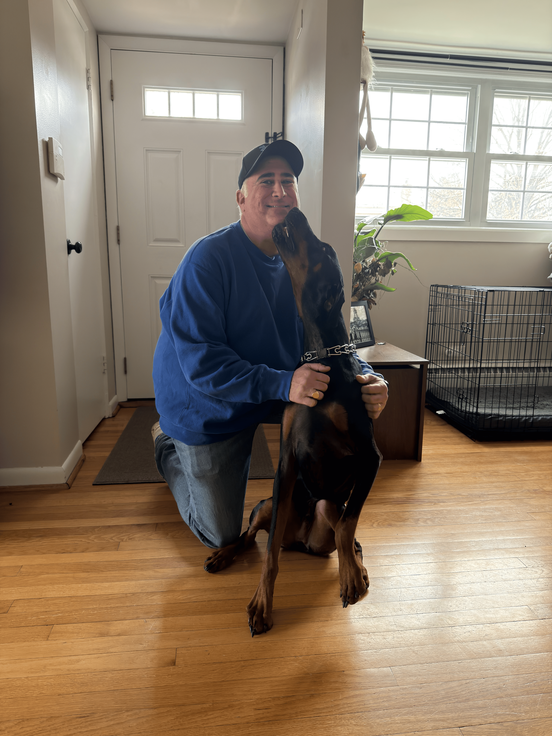 Person kneeling, hugging a Doberman Pinscher dog indoors near an entryway.
