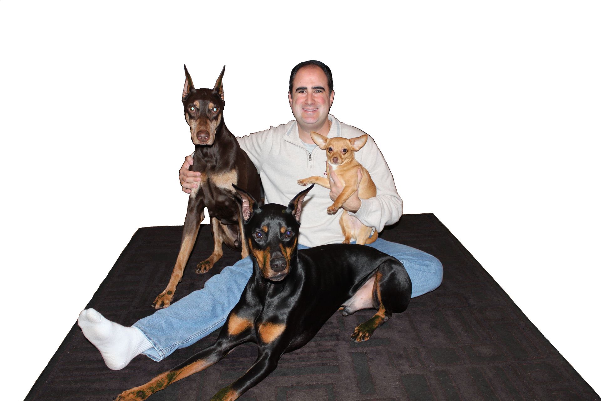 A man is sitting on a rug with three dogs
