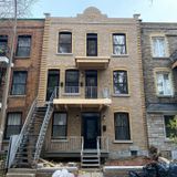 Un bâtiment en briques de trois étages avec un balcon et un escalier en bois. Il est flanqué de deux autres bâtiments.