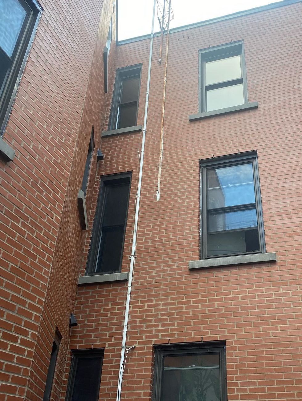 Extérieur d'un bâtiment en briques avec une échelle blanche fixée au mur, montant entre les fenêtres.