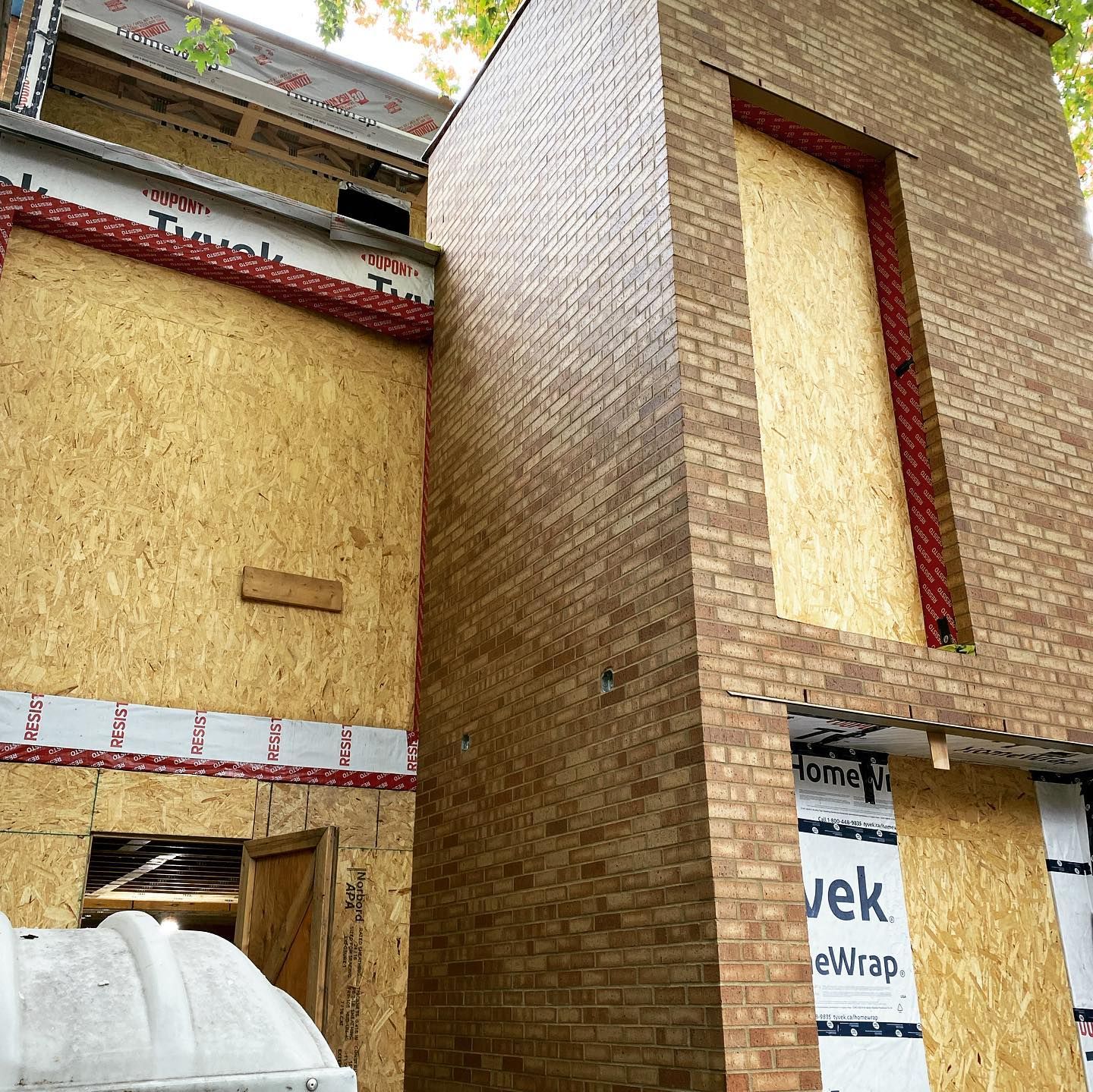 Un bâtiment en briques en construction, avec des ouvertures condamnées. La façade est revêtue d'un revêtement en bois et d'un revêtement en Tyvek.