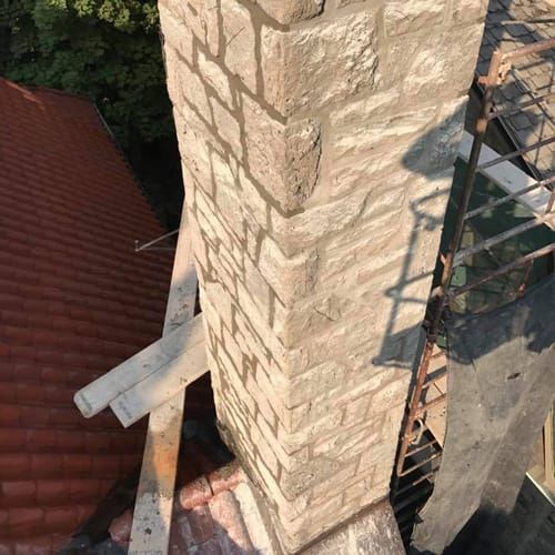 Gros plan d'une cheminée en pierre sur un toit, probablement en construction. La cheminée est grise et présente du mortier.