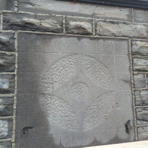 Mur de pierre avec un emblème circulaire sculpté comportant un cercle central et des formes rayonnantes en forme de pétales.