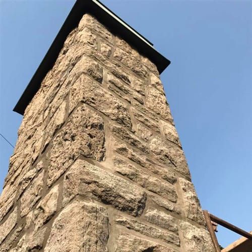 Pilier de pierre avec un capuchon sombre contre un ciel bleu clair.