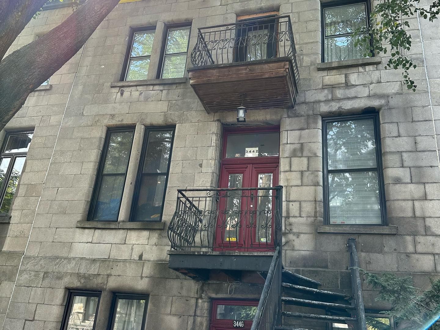 Bâtiment en pierre grise avec porte rouge et balcons en fer forgé. Un escalier en colimaçon noir mène à l'entrée.