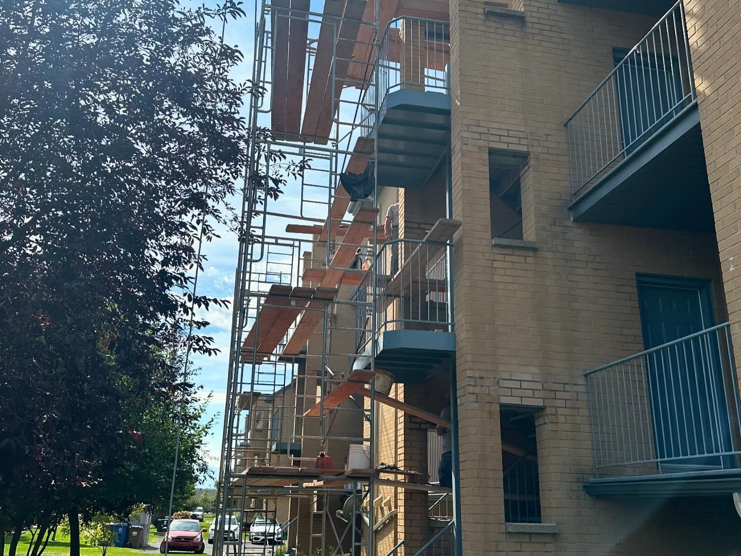 Un échafaudage entoure la façade en briques d'un immeuble d'habitation. Les ouvriers effectuent probablement des réparations ou des rénovations.