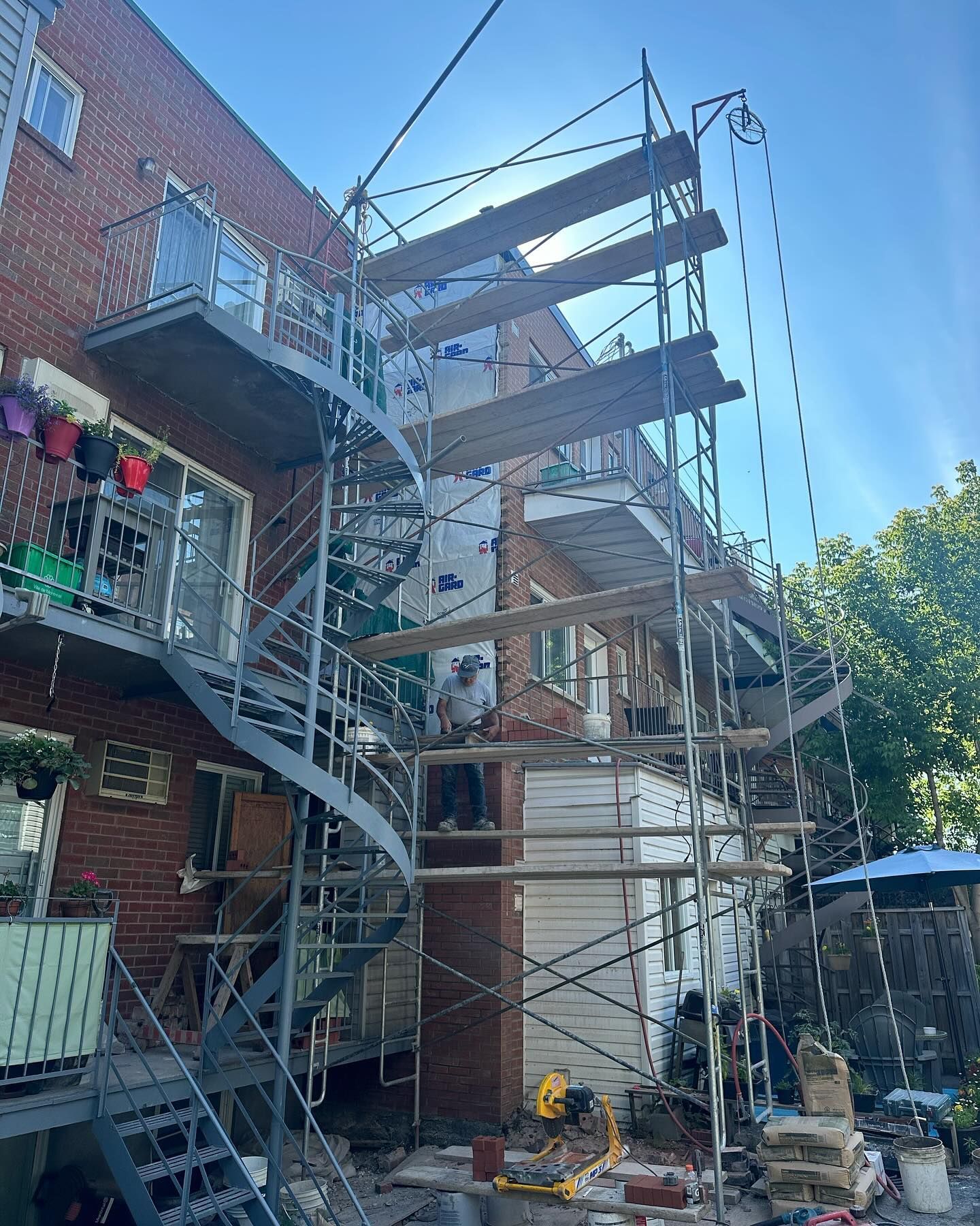 Extérieur d'un bâtiment en briques avec un échafaudage installé à côté ; un escalier en colimaçon en métal se trouve sur le côté gauche.