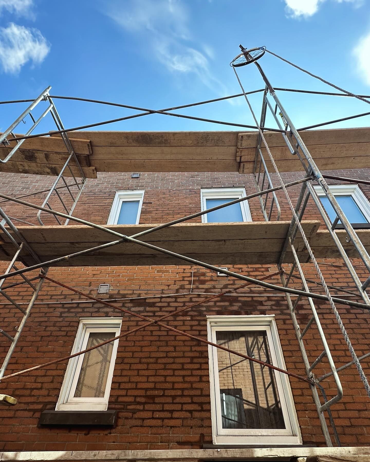 Façade d'un bâtiment en briques avec échafaudages, fenêtres à cadres blancs et ciel bleu clair. Les travaux semblent avoir commencé.