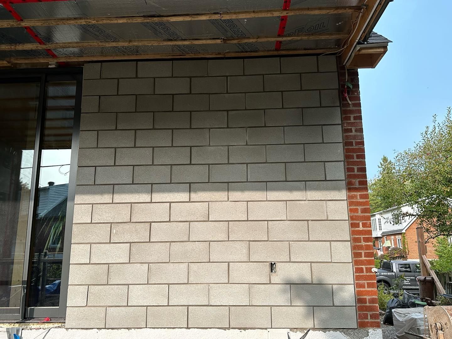 Mur extérieur en construction ; parpaings gris à côté d'un mur de briques. Une fenêtre et quelques matériaux de construction sont visibles.