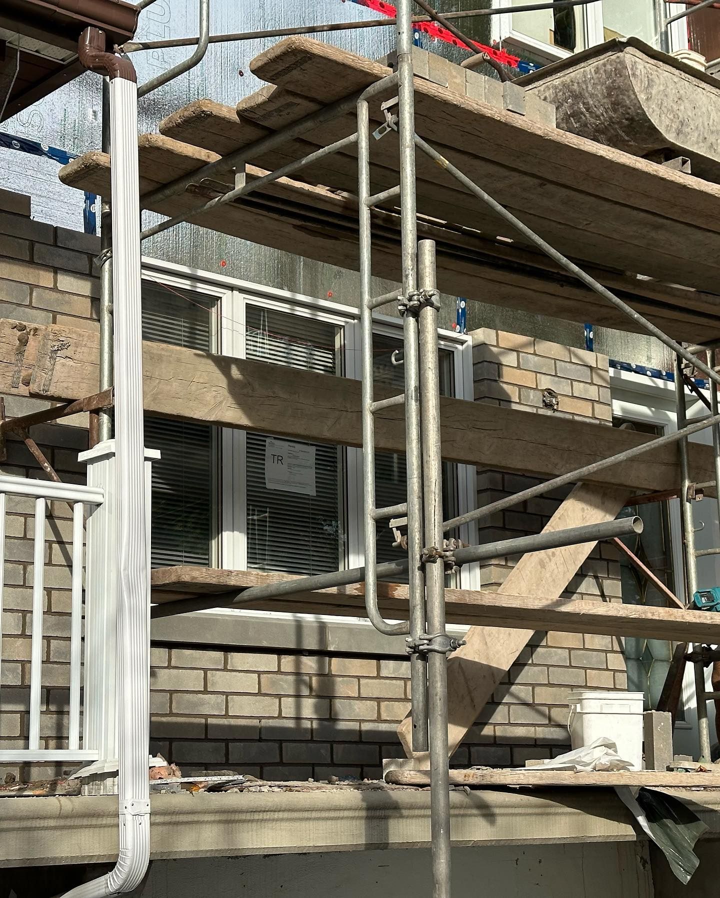 Échafaudage installé contre un bâtiment en briques avec une gouttière blanche, probablement pour la construction ou la réparation.